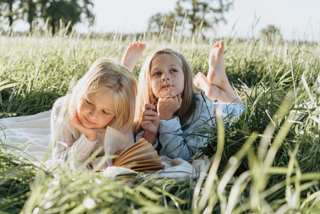 Zwei Kinder liegen im Gras und lächeln in die Kamera.