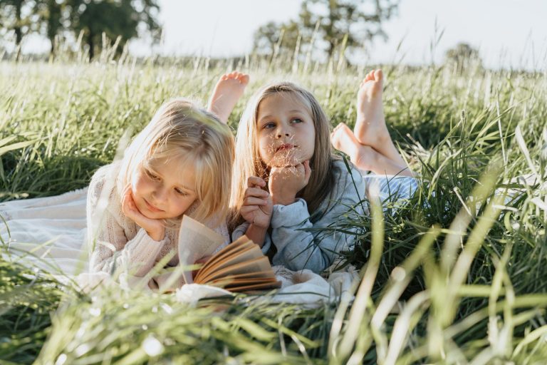 Zwei Kinder liegen im Gras und lächeln in die Kamera.