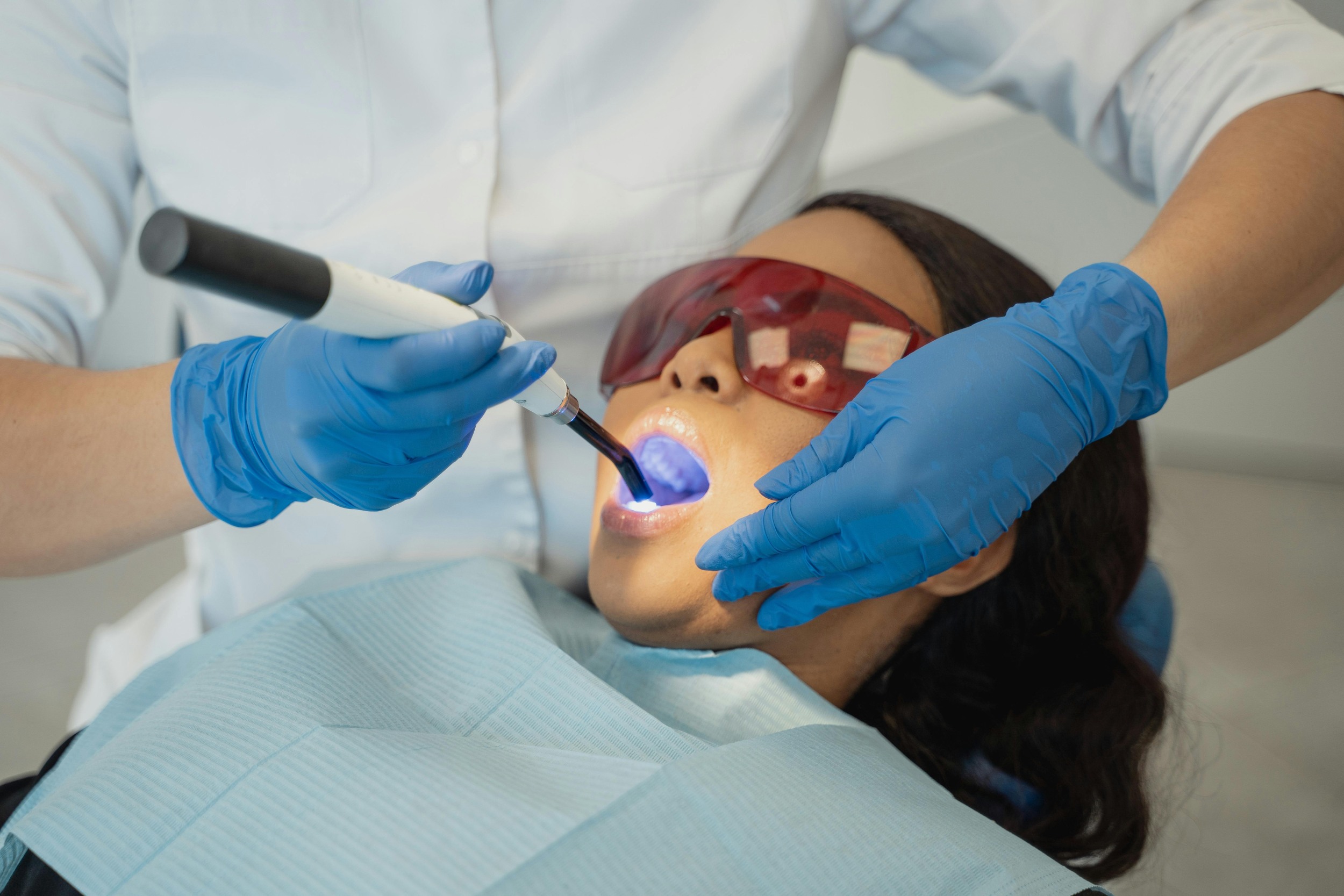 Zahnärztliche Füllungstherapie mit blauem Aushärtungslicht bei einer Patientin im Behandlungsstuhl.