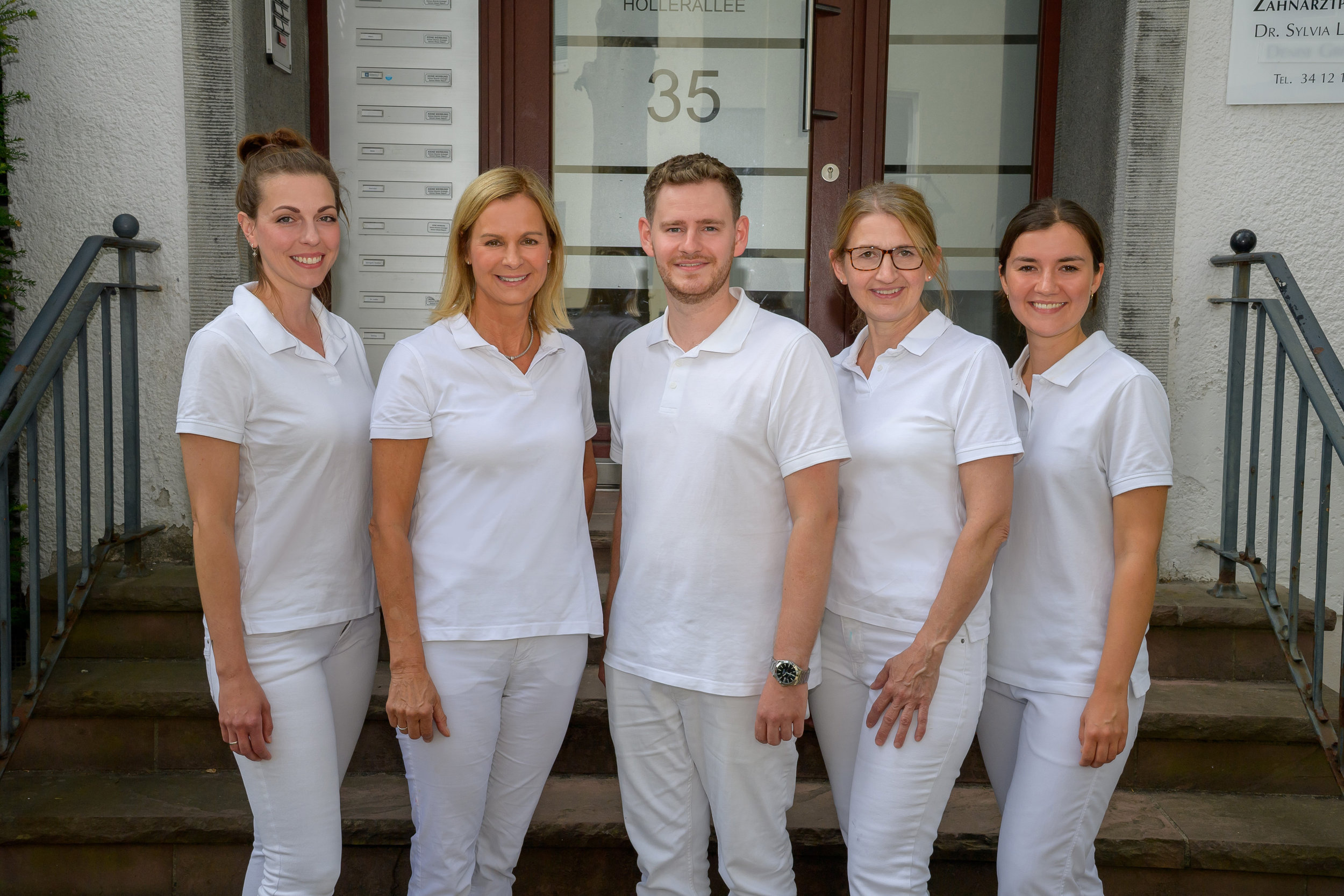 Behandlerteam der Zahnarztpraxis Hollerallee Malte Hoos steht vor dem Praxiseingang und lächelt in die Kamera