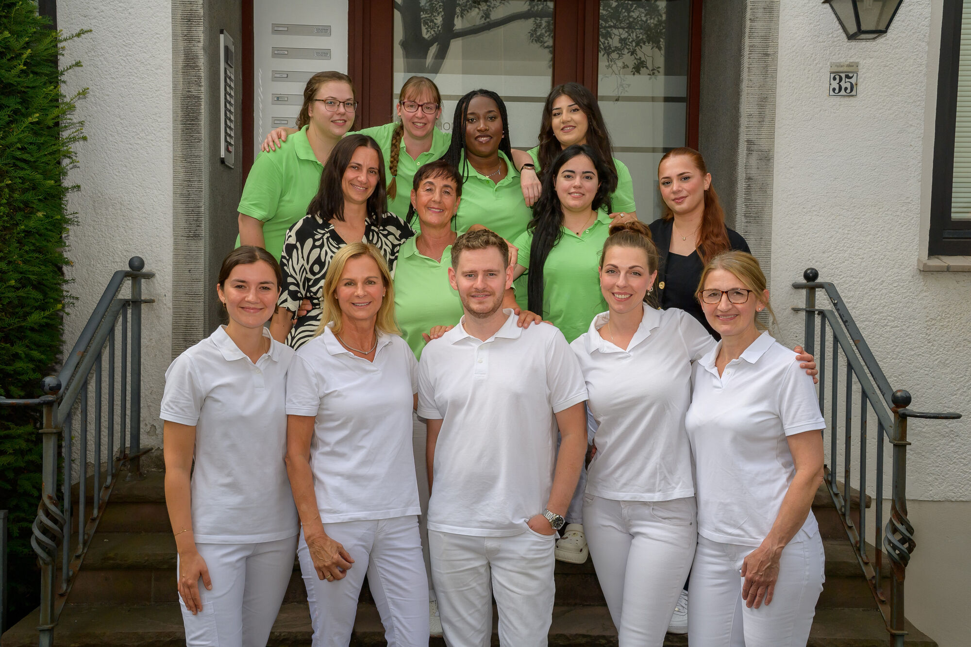 Team der Zahnarztpraxis Hollerallee Malte Hoos steht vor dem Praxiseingang und lächelt gemeinsam in die Kamera